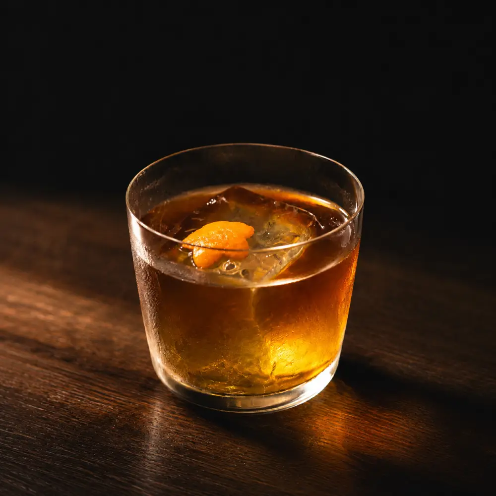 台南酒吧｜歧門酒吧茶調酒「沉澱的溫柔」，一杯深紅褐色調酒盛裝在古典矮杯中，內有一顆大冰球與橙皮裝飾。